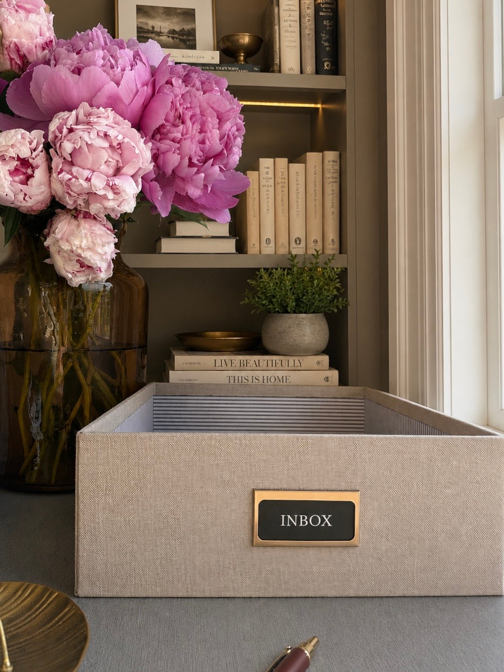 Beige storage box labeled 'INBOX' with pink flowers and books in the background